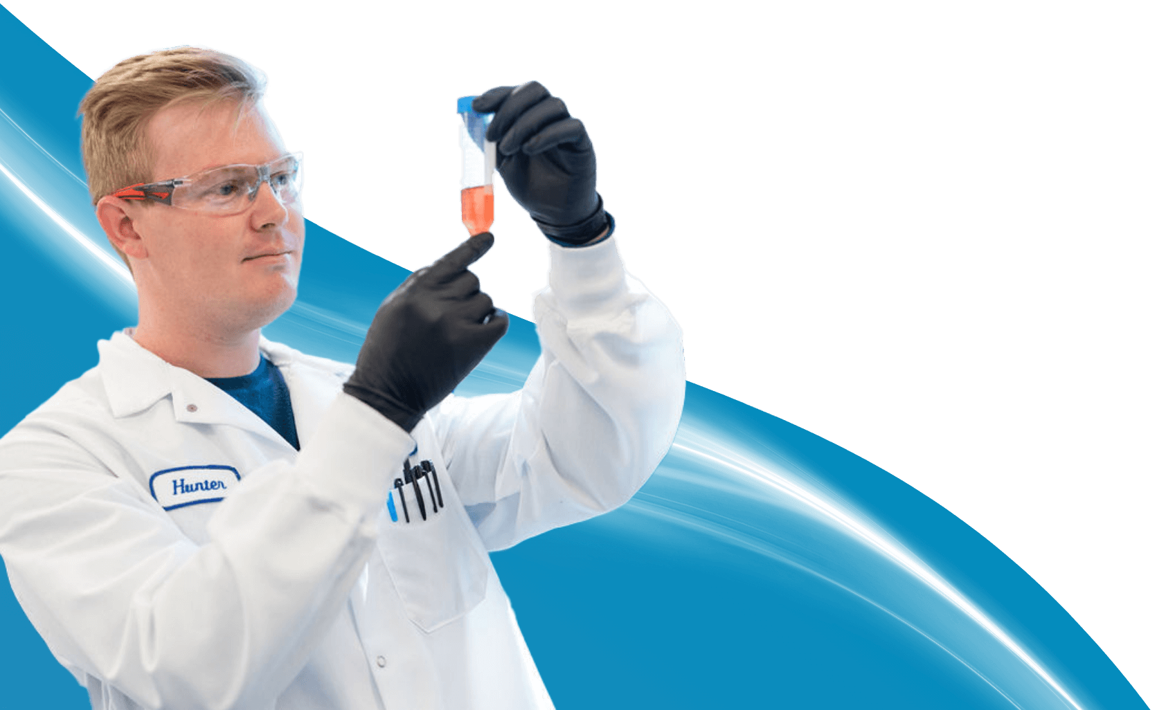 A cut-out image of a scientist wearing lab goggles, black gloves, and a white lab coat inspecting a tube of orange liquid, superimposed over a light blue wave background with a white light trail.