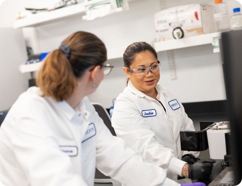 Two scientists in discussion in a lab look toward a computer screen.